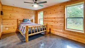 Une chambre dans une cabane en bois, avec un lit, un ventilateur de plafond et de grandes fenêtres.