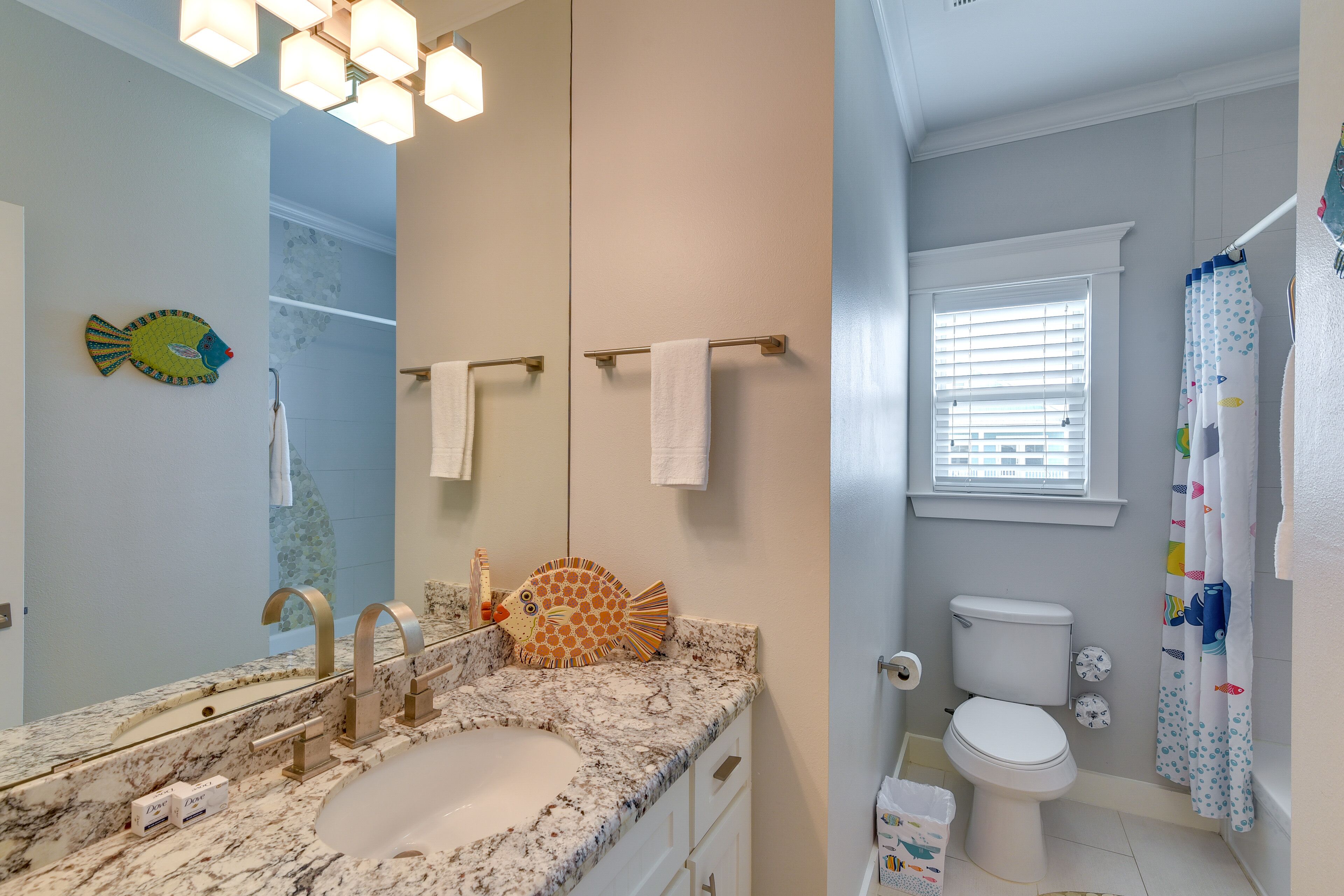 Une salle de bain avec un lavabo en marbre, des toilettes et un rideau de douche orné d’un motif de poissons.
