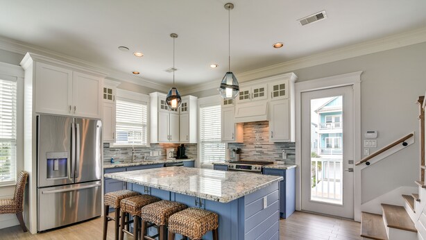 A modern kitchen with a central island, stainless steel appliances, and a staircase leading to a balcony. - Walk to Ocean! Group Beach House in Galveston (Galveston)