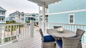 A covered outdoor area with wicker furniture and a round table, overlooking a row of blue buildings. - Walk to Ocean! Group Beach House in Galveston (Galveston)