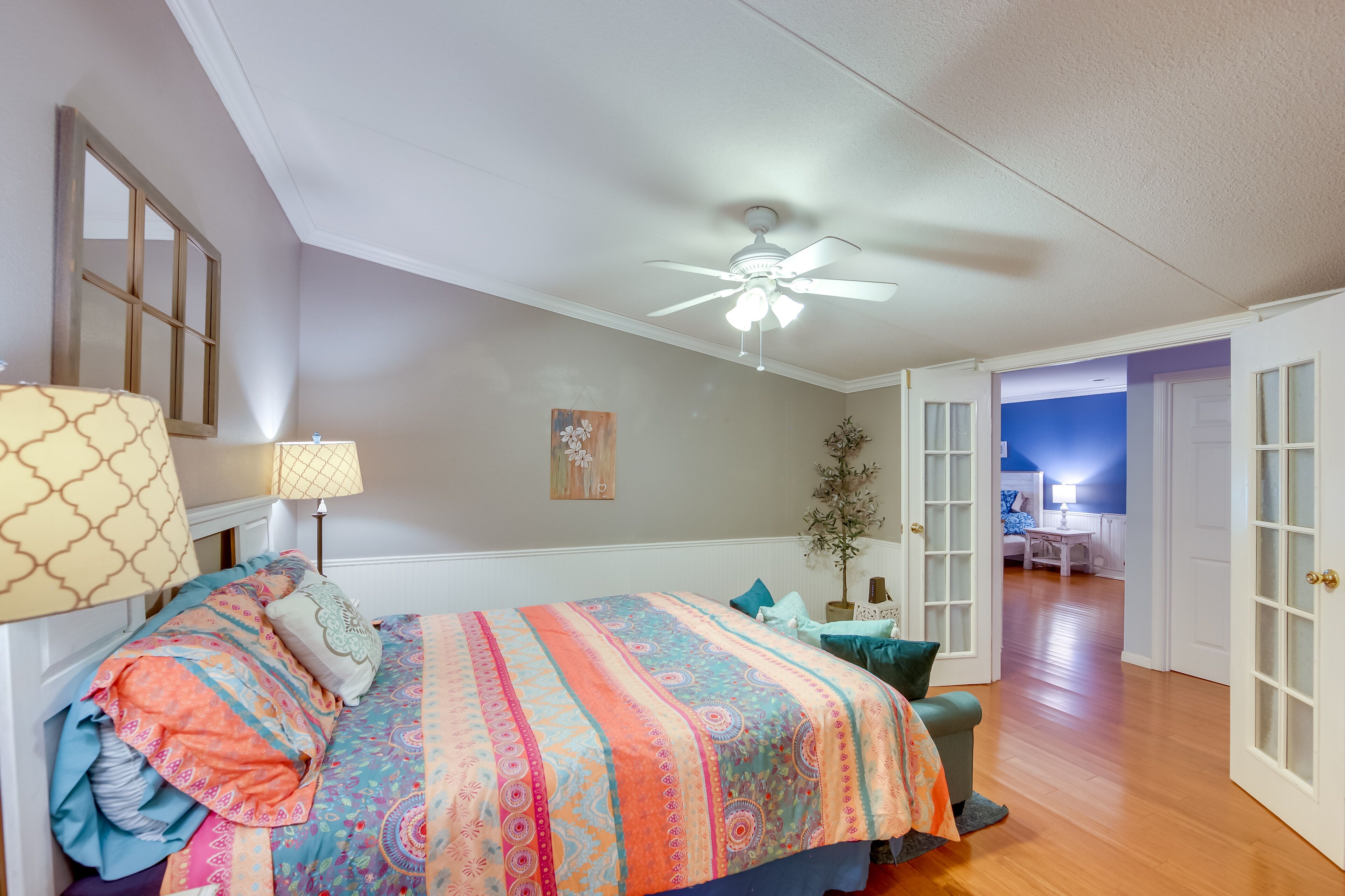 A bedroom with a large bed, a ceiling fan, a nightstand, and a view into another room.