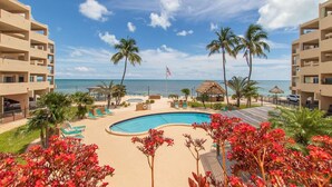 A resort pool area with palm trees, lounge chairs, and a view of the ocean. - Updated Unit with Beautiful Florida Bay Sunsets (Islamorada)
