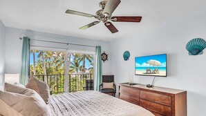 A bedroom with a bed, a desk, a television, and a balcony with a view of palm trees. - Updated Unit with Beautiful Florida Bay Sunsets (Islamorada)