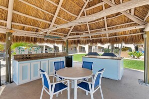 Une terrasse extérieure dotée d’un toit de chaume, d’une table ronde et de chaises bleues.