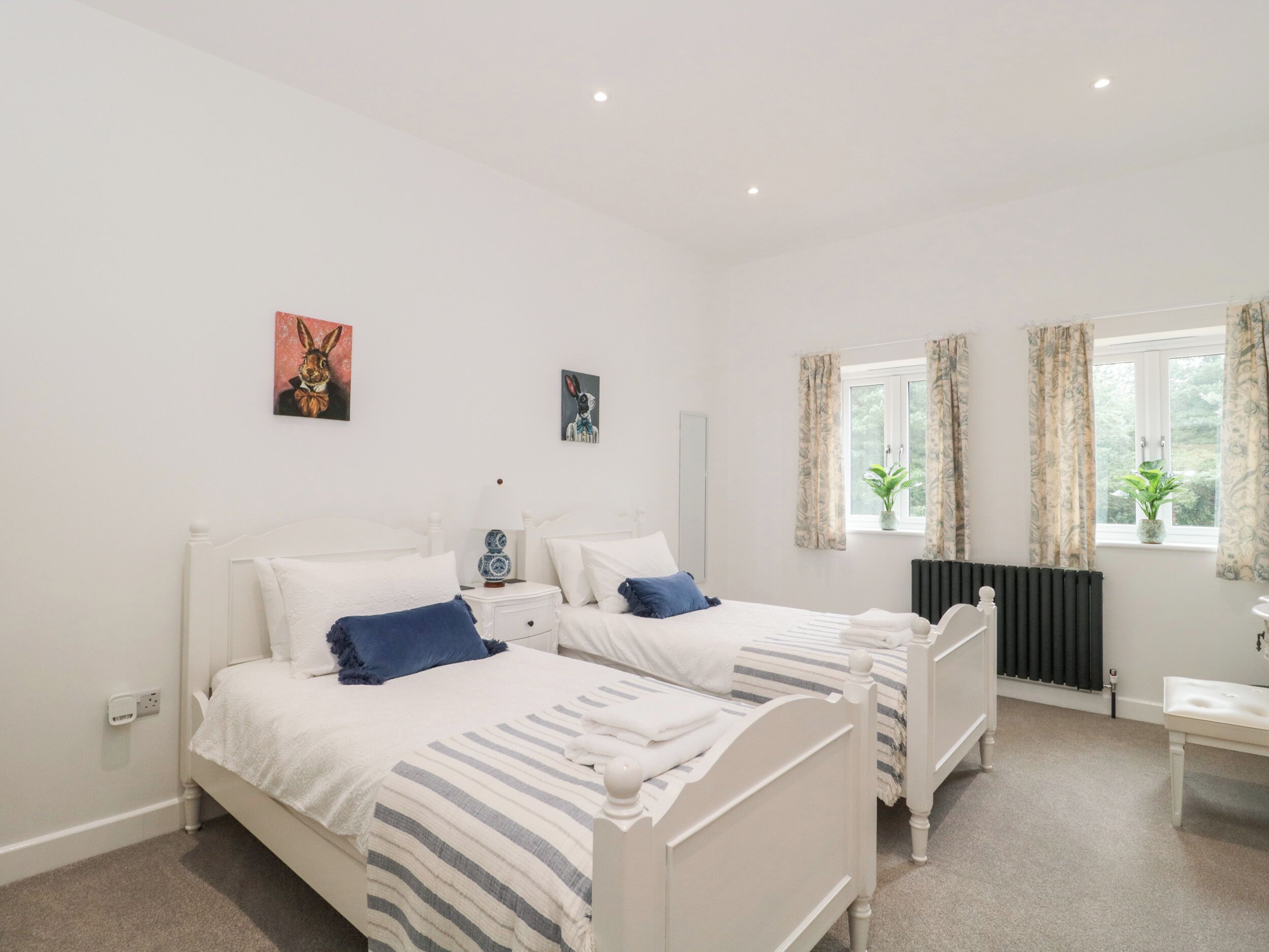 A bedroom with two single beds, a bedside table with a lamp, a radiator, and a window with curtains.