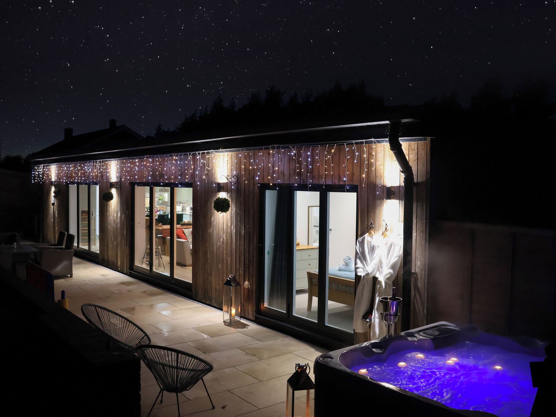 Un área de spa moderna al aire libre con hidromasaje, terraza de madera y luces colgantes.