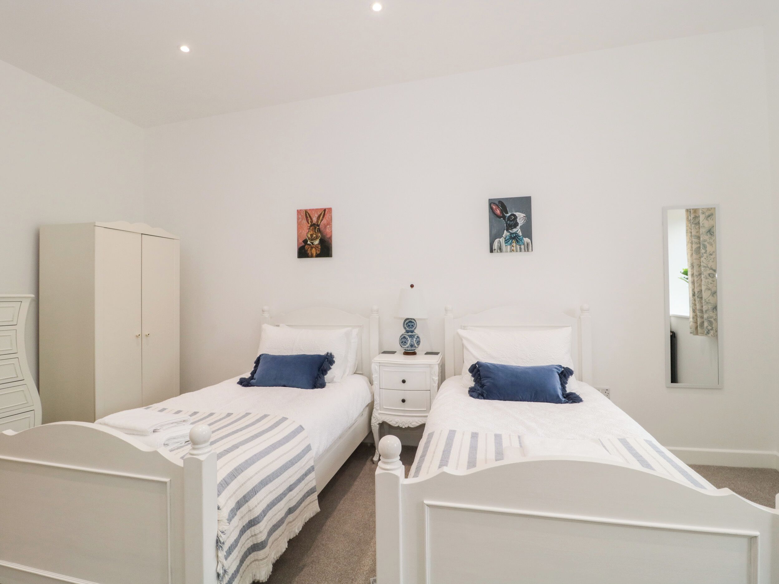 Ein Schlafzimmer mit zwei Einzelbetten, einem Kleiderschrank, Nachttischen und zwei an der Wand hängenden Bildern.