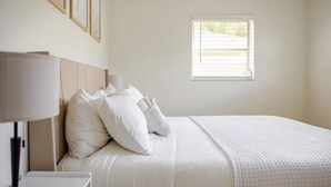 Un lit bien fait, avec une literie et des oreillers blancs, une lampe de chevet et une fenêtre équipée de stores.