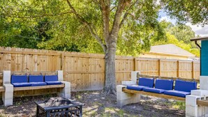 Un jardin avec une clôture en bois, deux bancs bleus avec des coussins et une petite table.