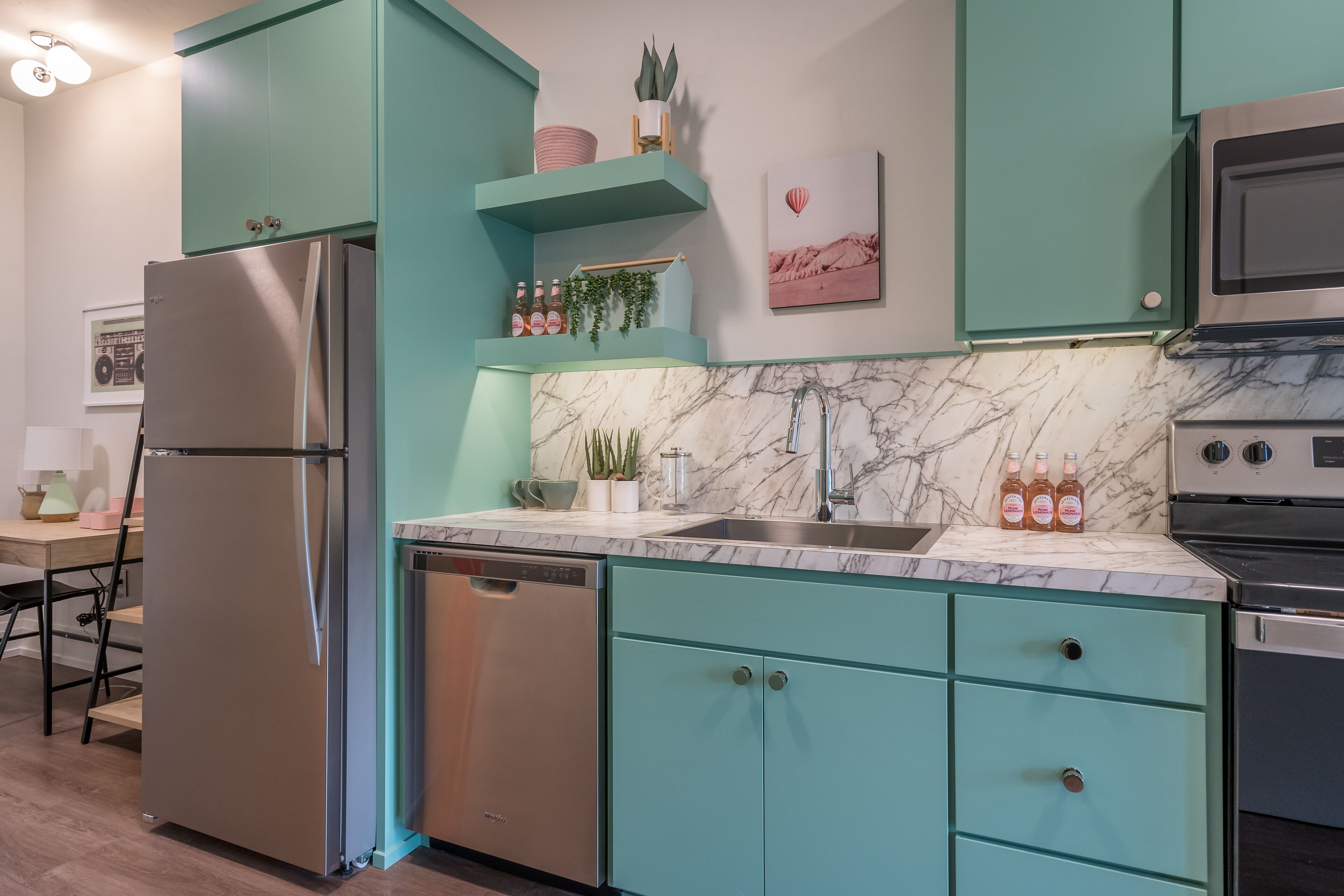 Une cuisine avec des armoires de couleur turquoise, un réfrigérateur en acier inoxydable, un lave-vaisselle, un plan de travail en marbre, un évier et une cuisinière.