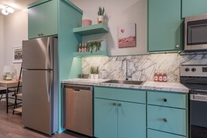 Una cocina con armarios color turquesa, un refrigerador de acero inoxidable, lavavajillas, encimera de mármol, un fregadero y una estufa.