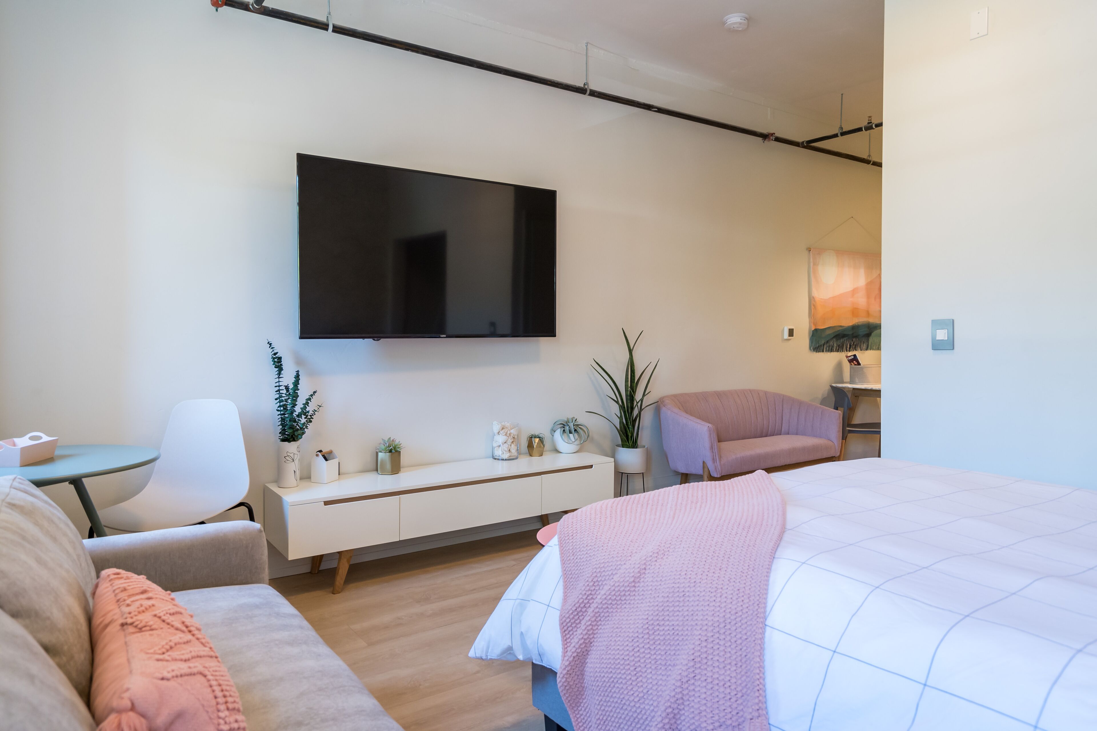 A modern bedroom with a large bed, a TV mounted on the wall, a small desk, and a chair.
