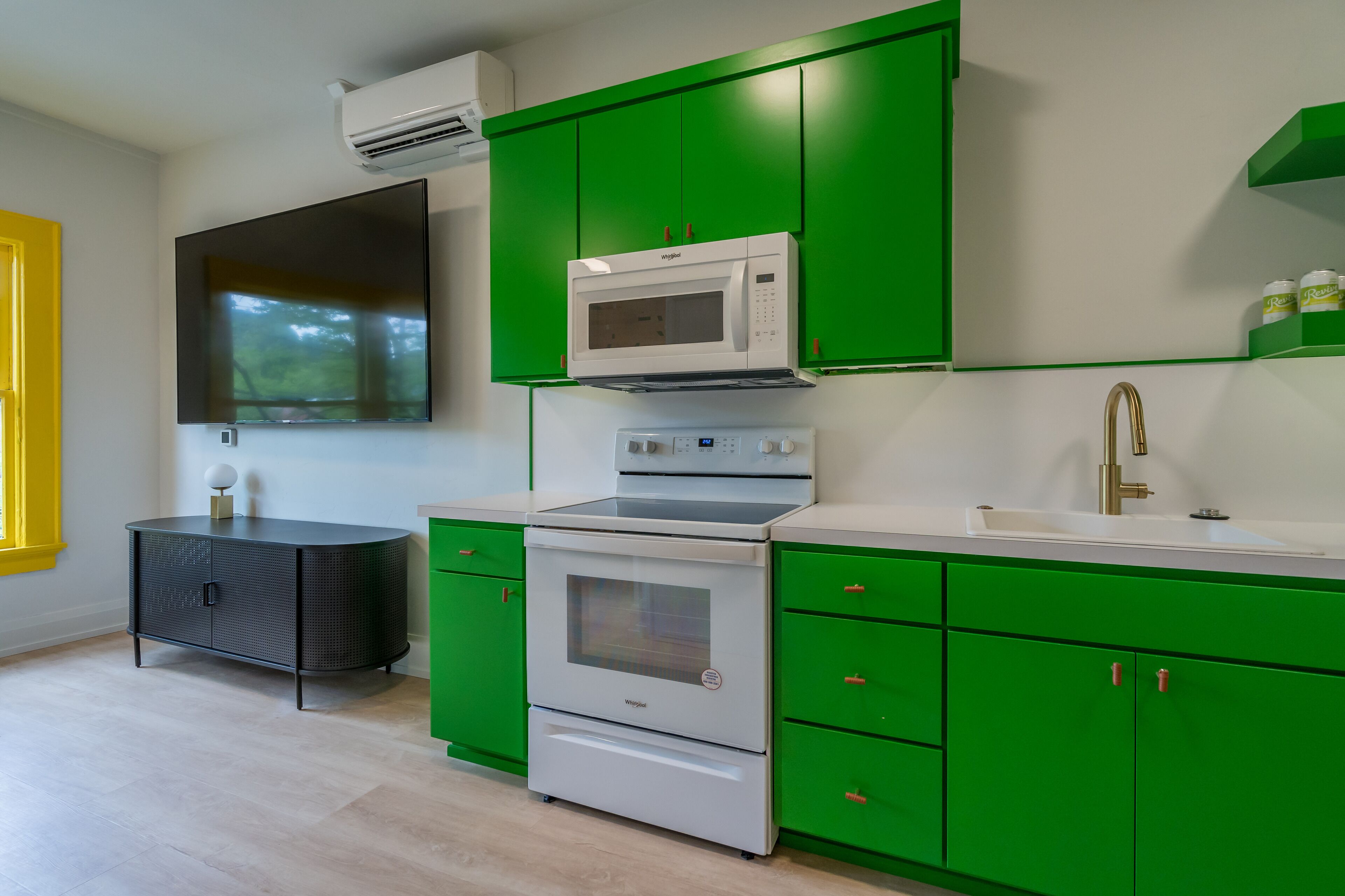 Una cocina moderna con armarios verdes, una estufa blanca, un microondas y un ventanal grande.