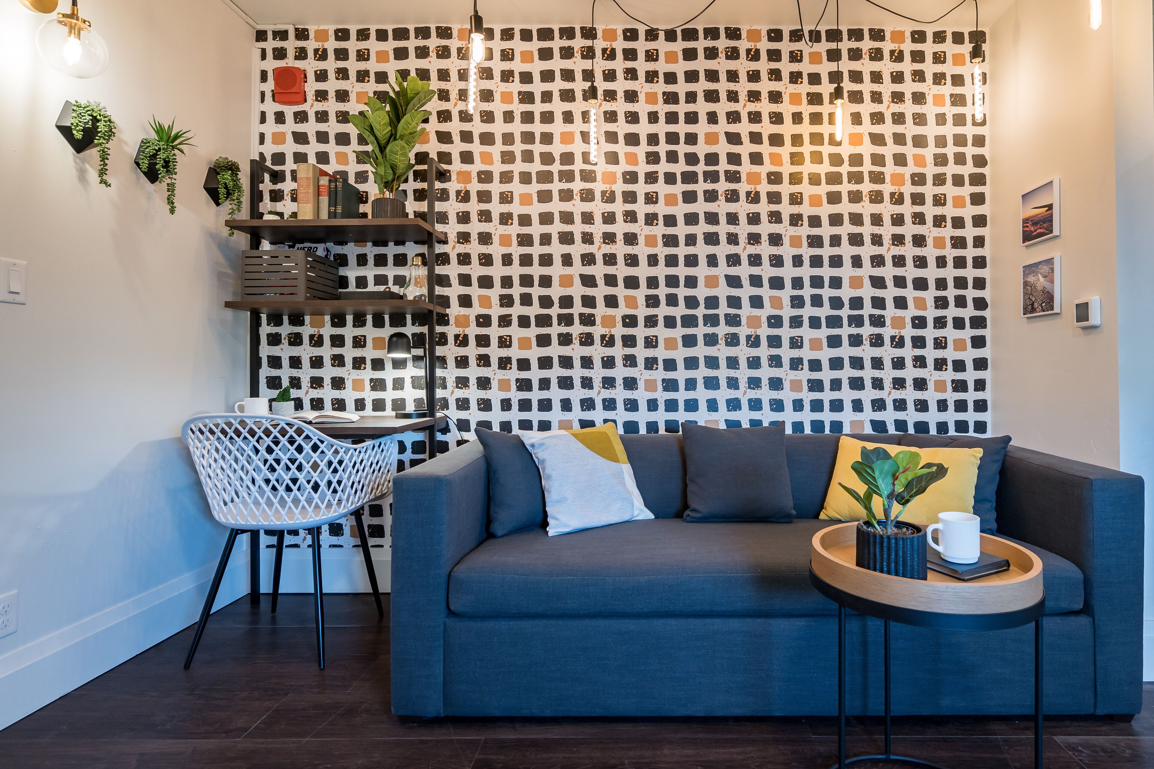 Una sala de estar moderna con una pared estampada, un sofá gris, una silla blanca y una mesita de madera con una planta y una taza.