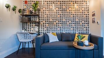 Una sala de estar moderna con una pared estampada, un sofá gris, una silla blanca y una mesita de madera con una planta y una taza.