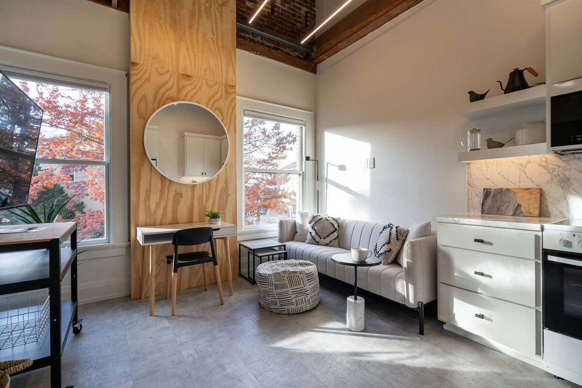 A modern kitchen with a wooden accent wall, a round mirror, a dining area with a table and chairs, and a sofa with a coffee table.