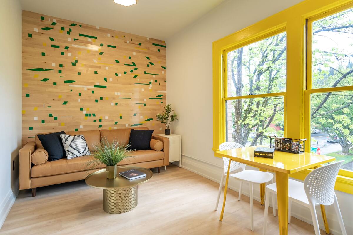 A modern living room with a wooden wall, a tan sofa, a round coffee table, and a yellow window.