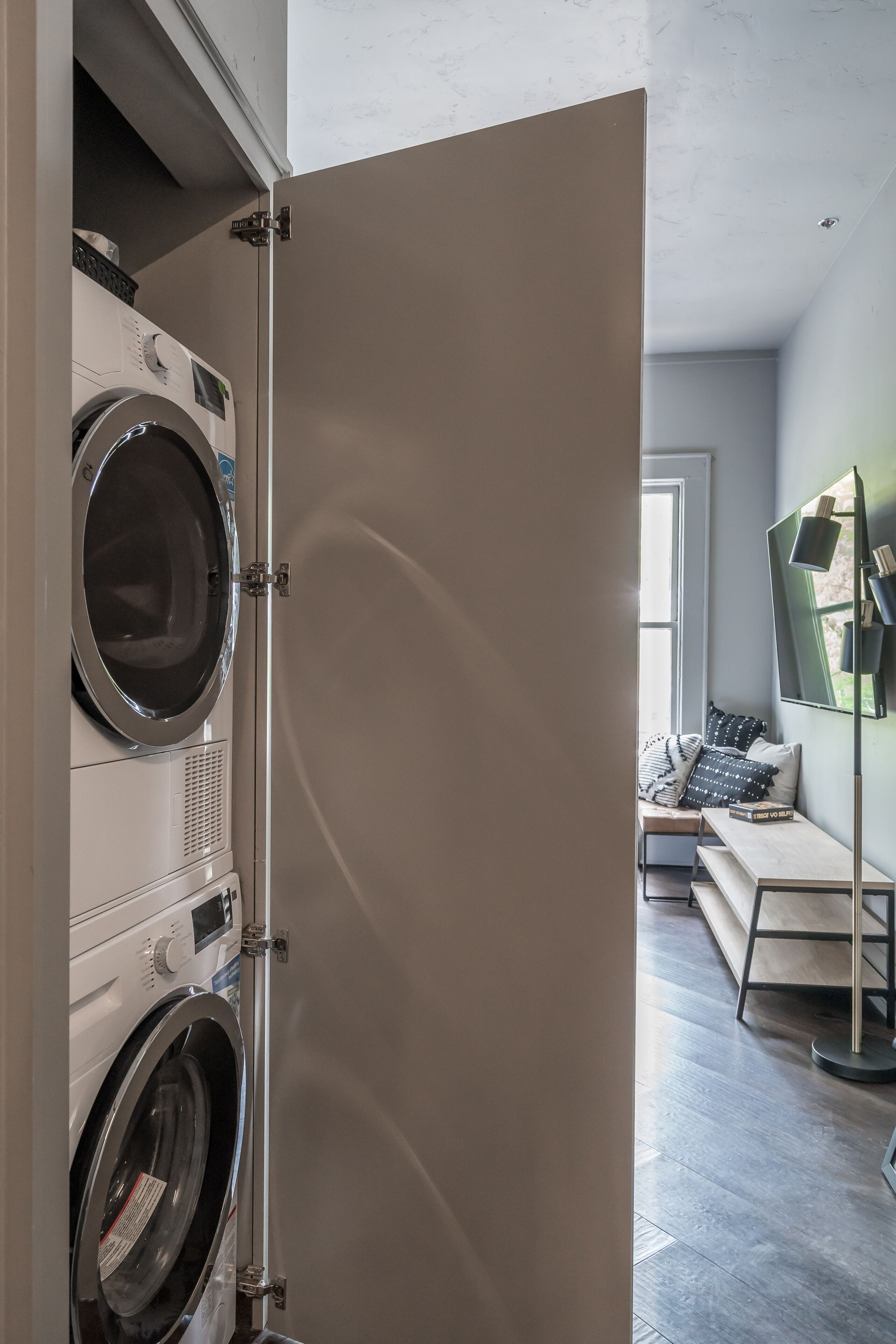 A laundry room with stacked washers and dryers, a bench, and a large mirror.