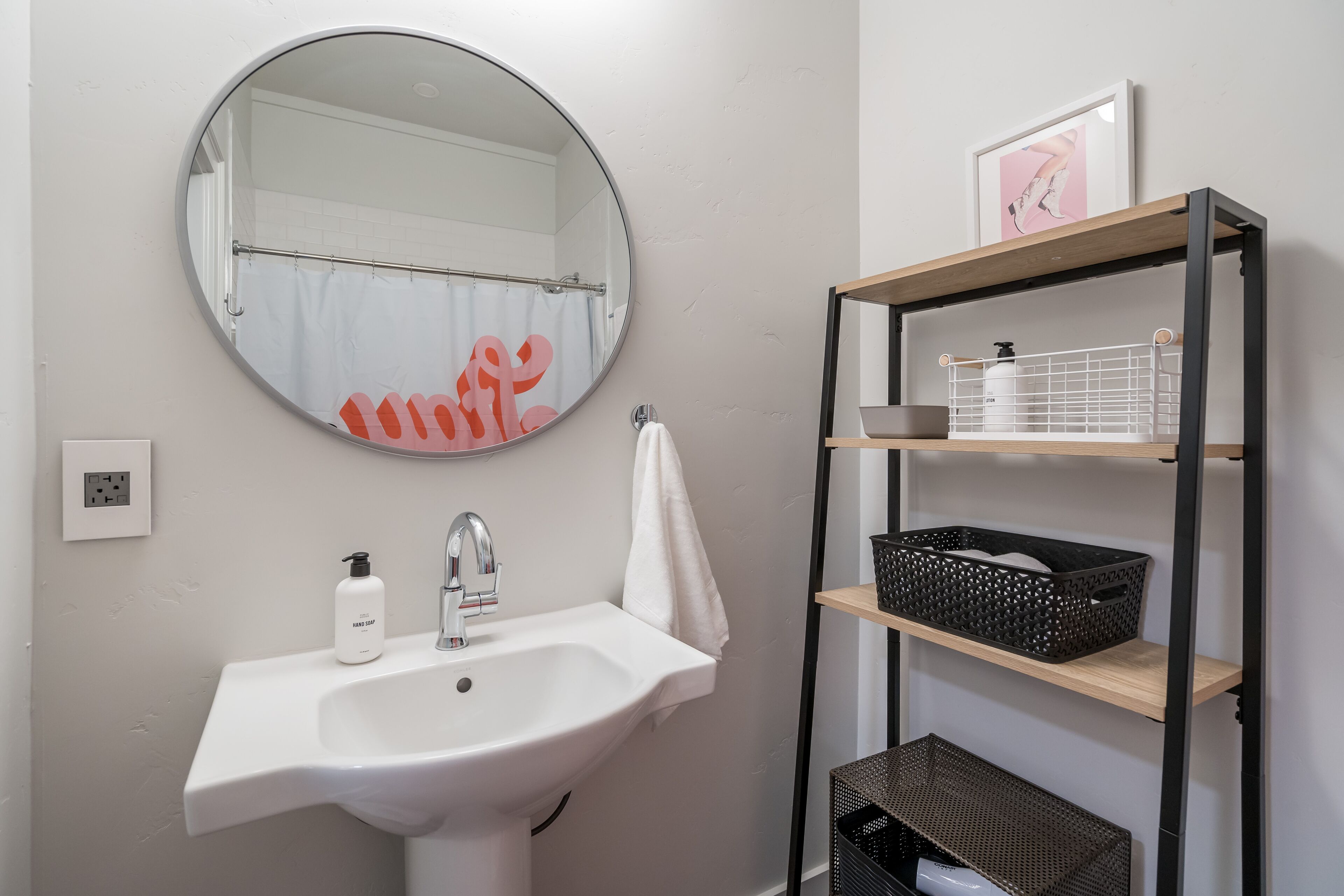 A bathroom with a white sink, a round mirror, a towel hanging on the wall, and a shelf with baskets.