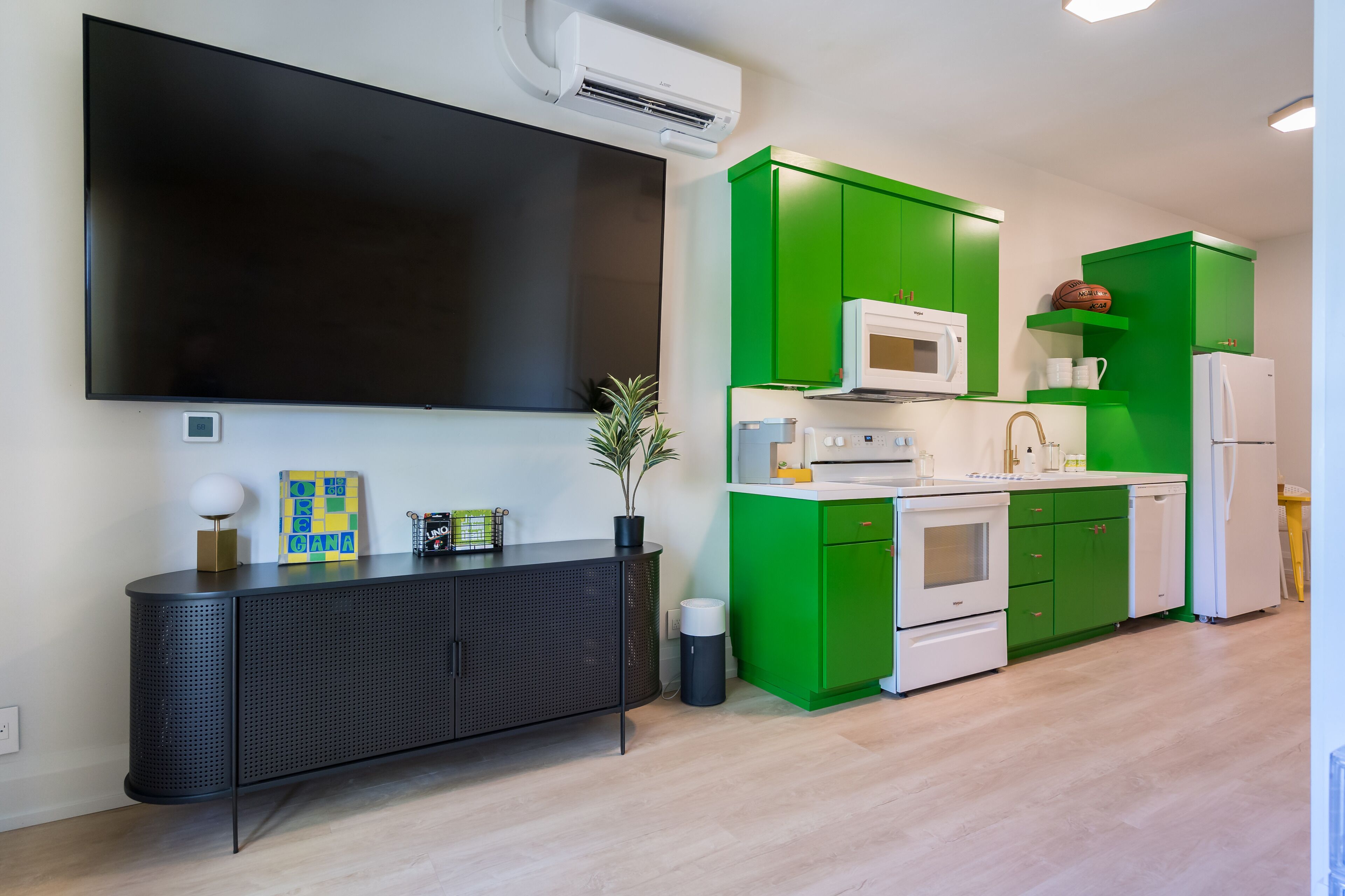 Eine moderne Küche mit grünen Schränken, einem weißen Kühlschrank und einem an der Wand befestigten Flachbildfernseher.