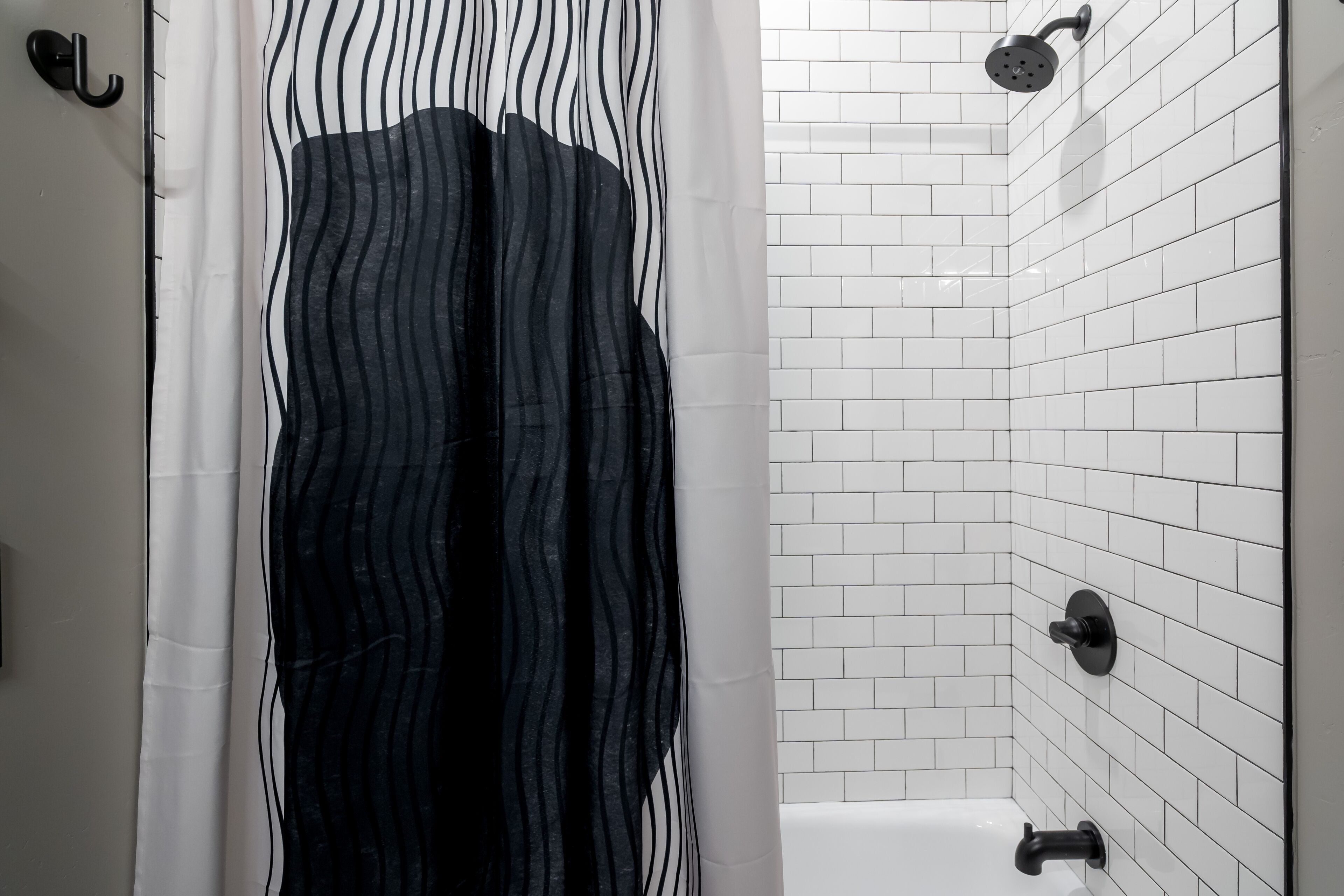 A bathroom with white tiled walls, a black shower curtain, and a white bathtub.