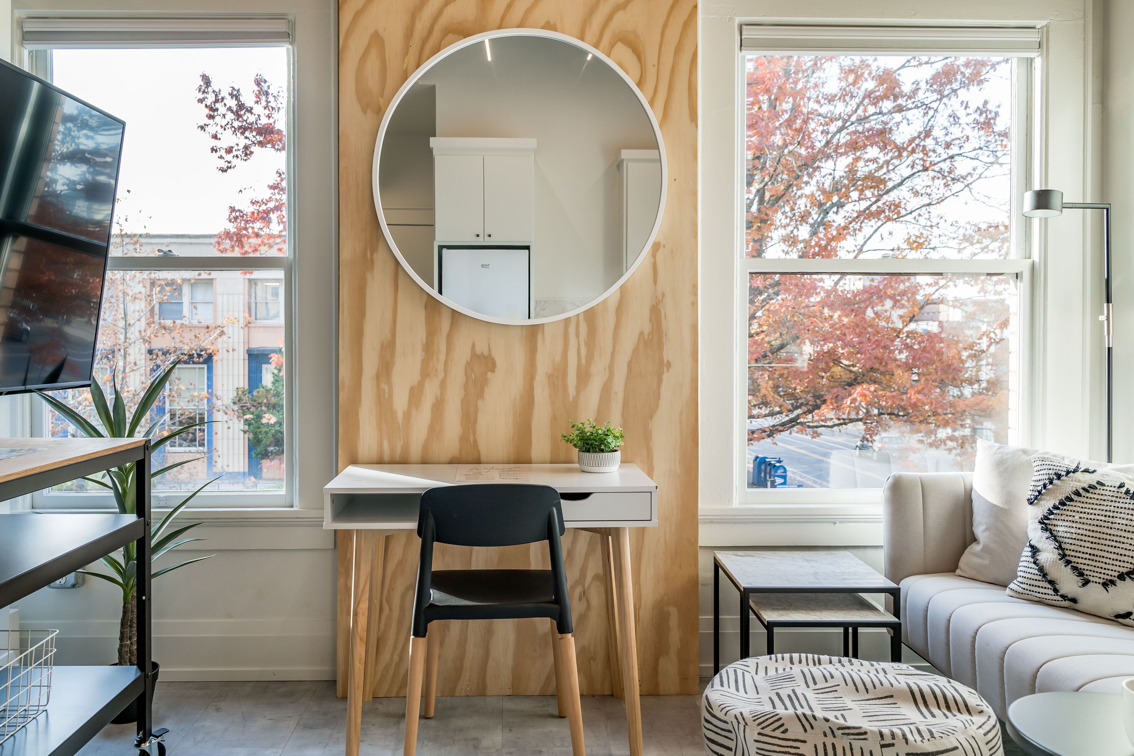 A modern room with a desk, chair, round mirror, and a sofa with a patterned cushion.