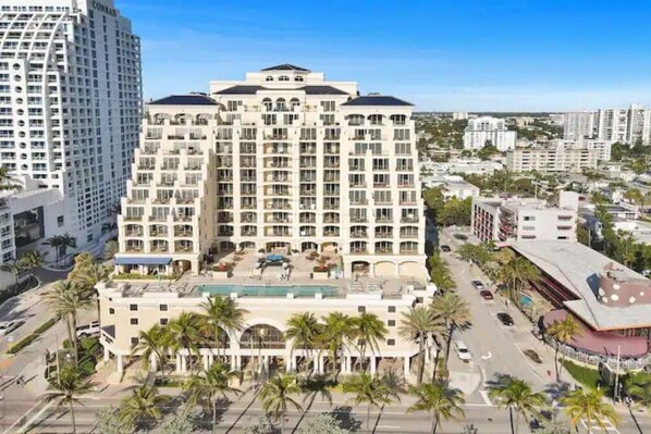 A multi-story hotel with a central courtyard, surrounded by palm trees and adjacent to a road.