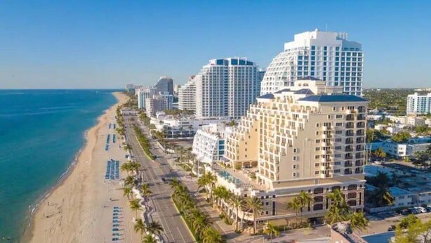 Un hotel costero con varios edificios altos, una playa y palmeras.