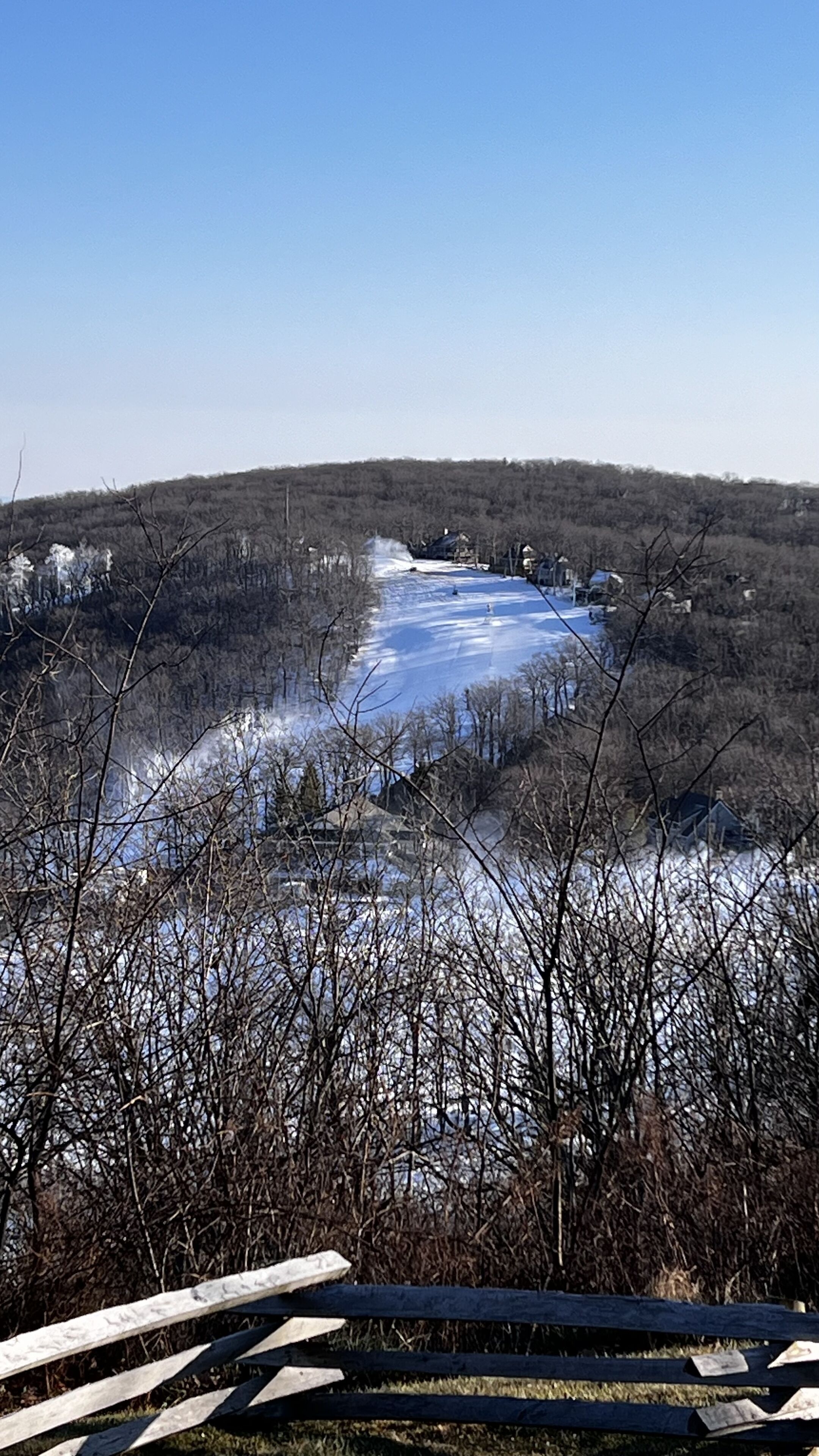 A view of a frozen lake with houses in the background and leafless trees in the foreground.