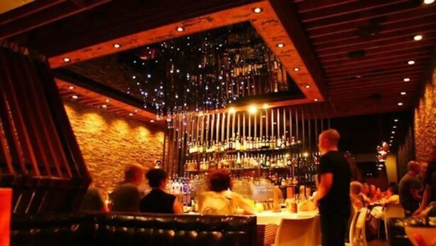 Een bar met een bakstenen muur, houten plafond en hangende lampen.