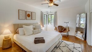 Een moderne slaapkamer met een groot bed, plafondventilator en uitzicht op het groen door een raam.