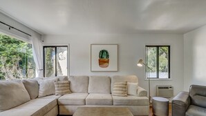 Een moderne woonkamer met een hoekbank, een bijzettafeltje met een mand, en een wanddecoratie van een cactusprent.