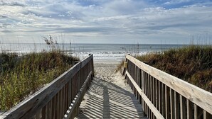 Une promenade en bois menant à une plage, avec un ciel nuageux.