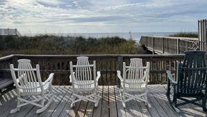 Une terrasse en bois avec trois fauteuils à bascule donnant sur une plage.