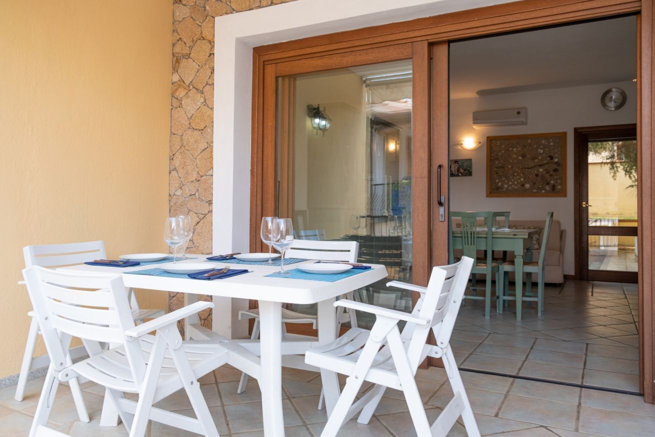 A dining area with a white table and chairs, a glass door leading to a balcony, and a stone wall.