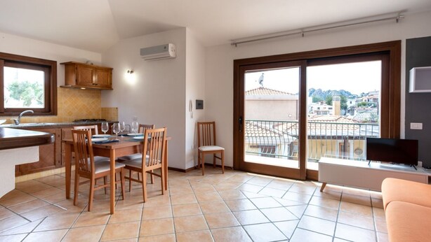 A kitchen with a dining table, chairs, and a balcony with a TV. - Mirto 4 Apartment (Santa Maria Navarrese)