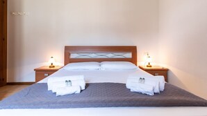A neatly made double bed with a grey quilt, two bedside tables with lamps, and a wooden headboard. - Mirto 4 Apartment (Santa Maria Navarrese)