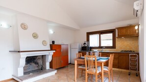 A compact kitchen with a fireplace, wooden cabinets, a dining table with chairs, and a window providing natural light. - Mirto 4 Apartment (Santa Maria Navarrese)