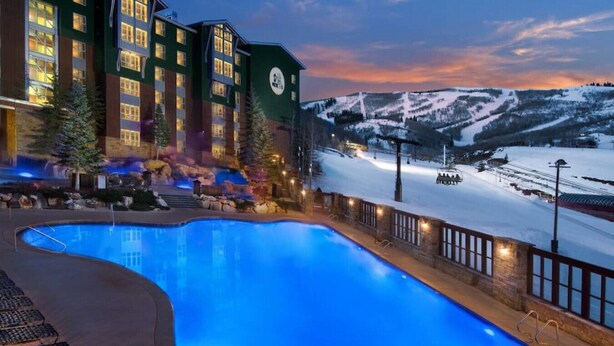 Un hôtel doté d’une piscine, entouré de montagnes enneigées, et offrant une vue sur le ciel nocturne.