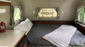 Ein kompaktes Wohnmobil-Interieur mit einem Bett, einem kleinen Tisch und einem Fenster mit Vorhängen.