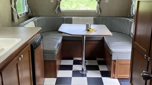 Eine kompakte Küchenzeile in einem Wohnmobil mit kariertem Boden, einem Esstisch und einer eingebauten Sitzbank.