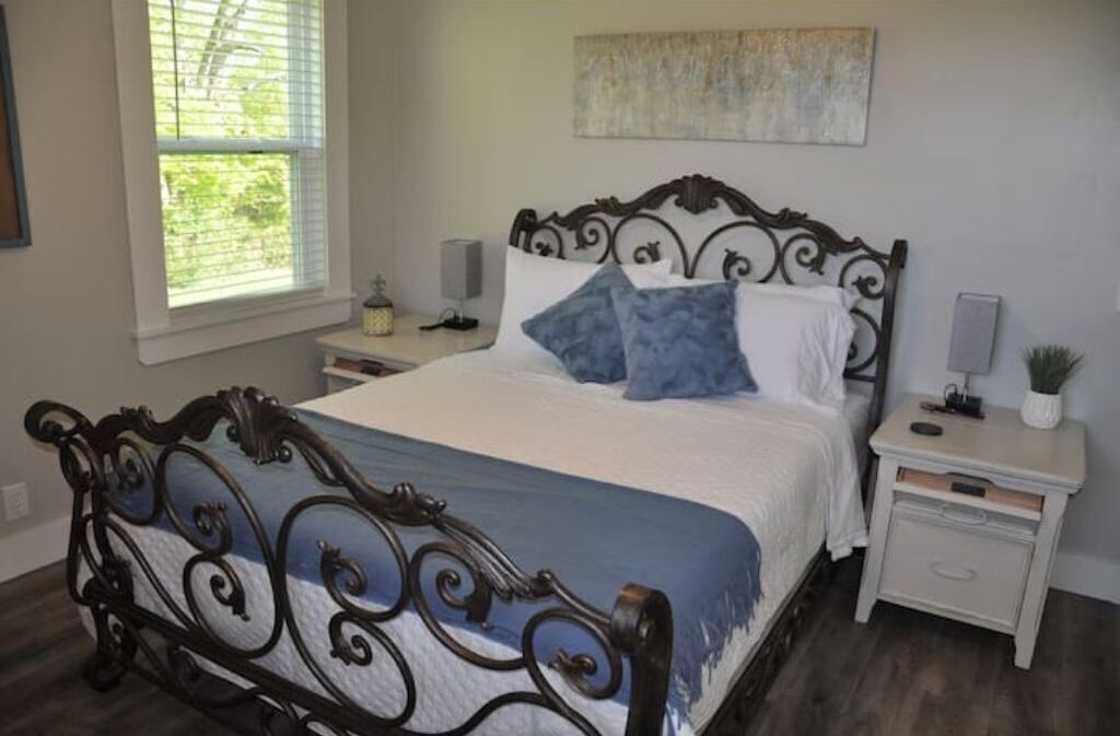 A bedroom with a bed, nightstands, a window, and a wall-mounted artwork.