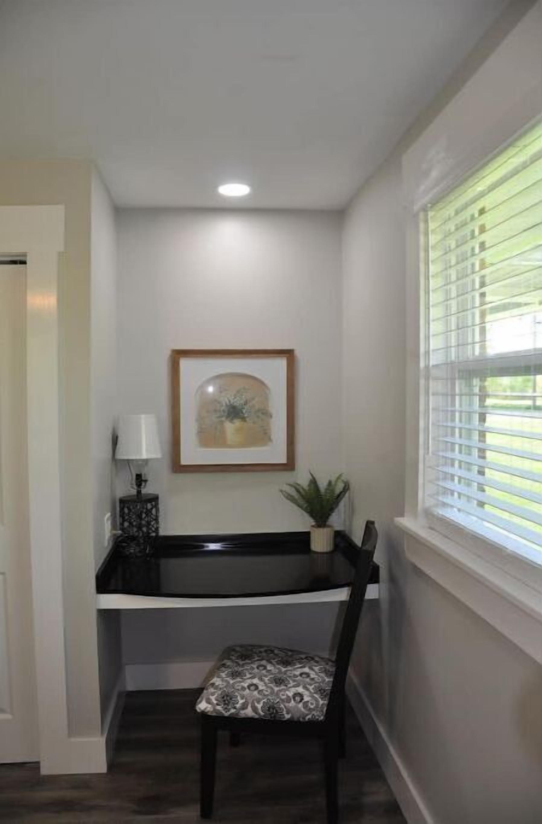 A corner room with a desk, chair, framed artwork, and a window with blinds.