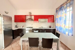 A kitchen with red cabinets, a stainless steel refrigerator, a gas stove, and a dining table with chairs. - P007 - Porto Recanati, large three-room apartment with parking near the sea (Porto Recanati)
