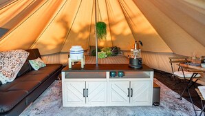 A cozy tent with a sofa, a small table with a kettle, and a hanging plant.