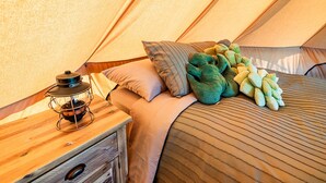 A cozy tent interior with a bed, pillows, a lantern, and a blanket.