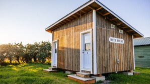 A rustic wooden bath house with a white door and a sign reading "BATH HOUSE" on the side.