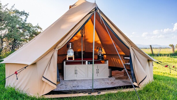 A dome-shaped tent with a central table and cabinets, set in a grassy field.