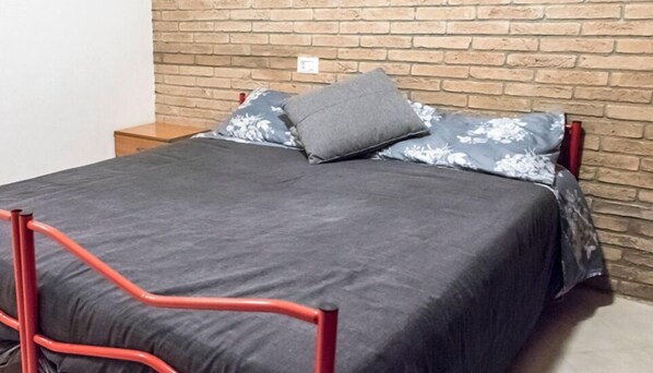 A bed with a grey bedspread and floral pillows, a red metal frame, and a brick wall. - SE010 - Senigallia, one bedroom apartment on the sea with beach (Senigallia)