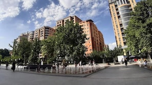 Una plaça pública amb una font, envoltada d'arbres i edificis alts.